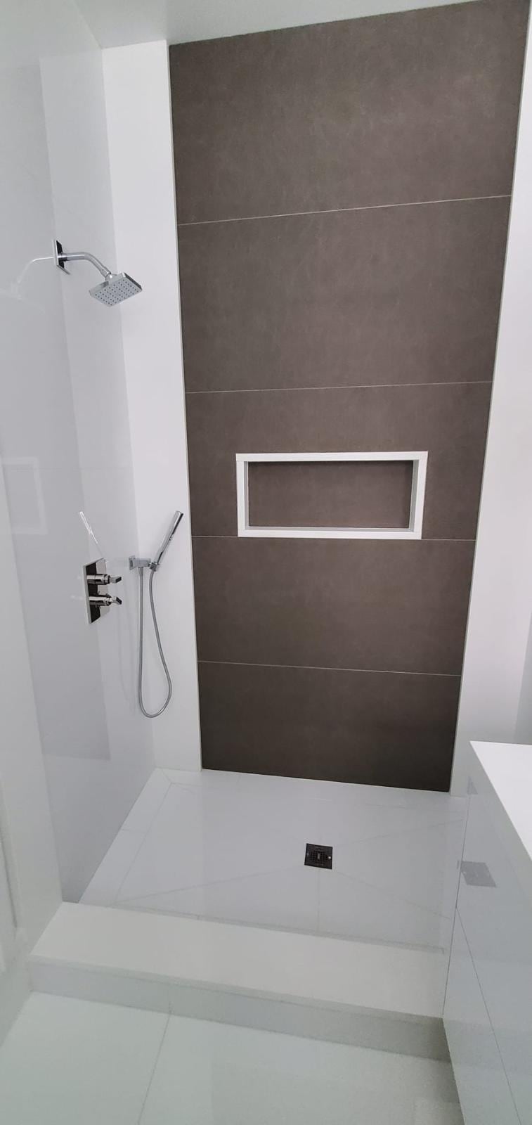 Tall walk-in shower with a dark large-format tile wall, a recessed niche and a white tile floor