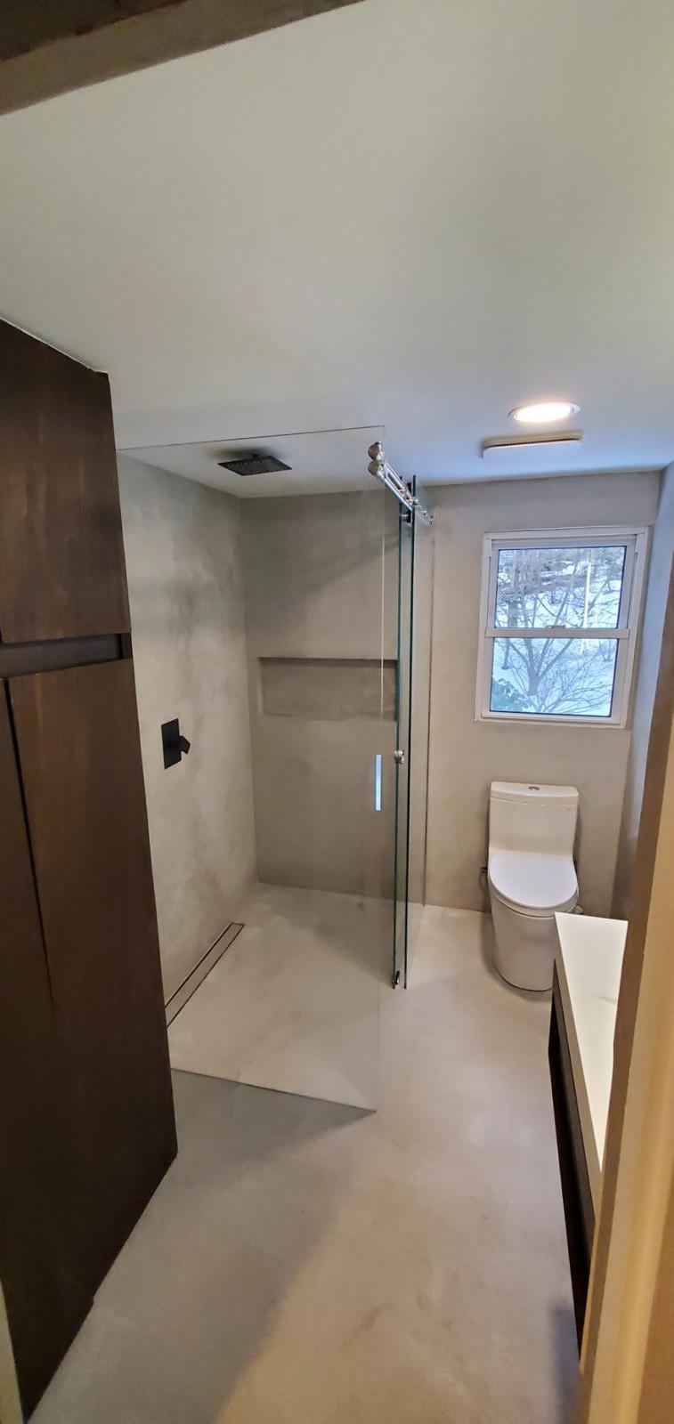 Walk-in shower with linear drain and glass panel in a modern bathroom with a dark wood cabinet