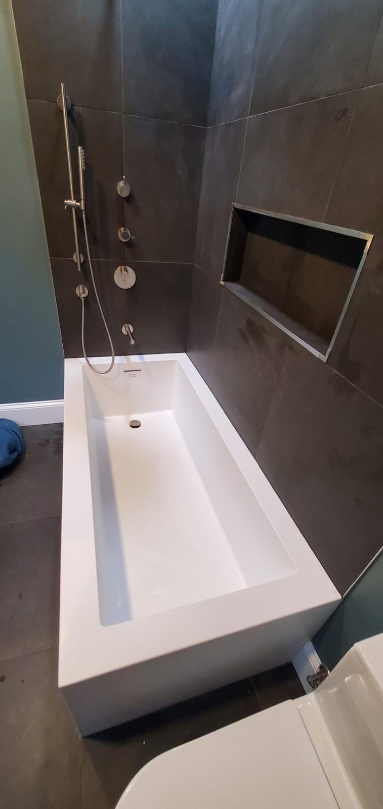 Deep soaking tub against large-format dark tile with a built-in niche