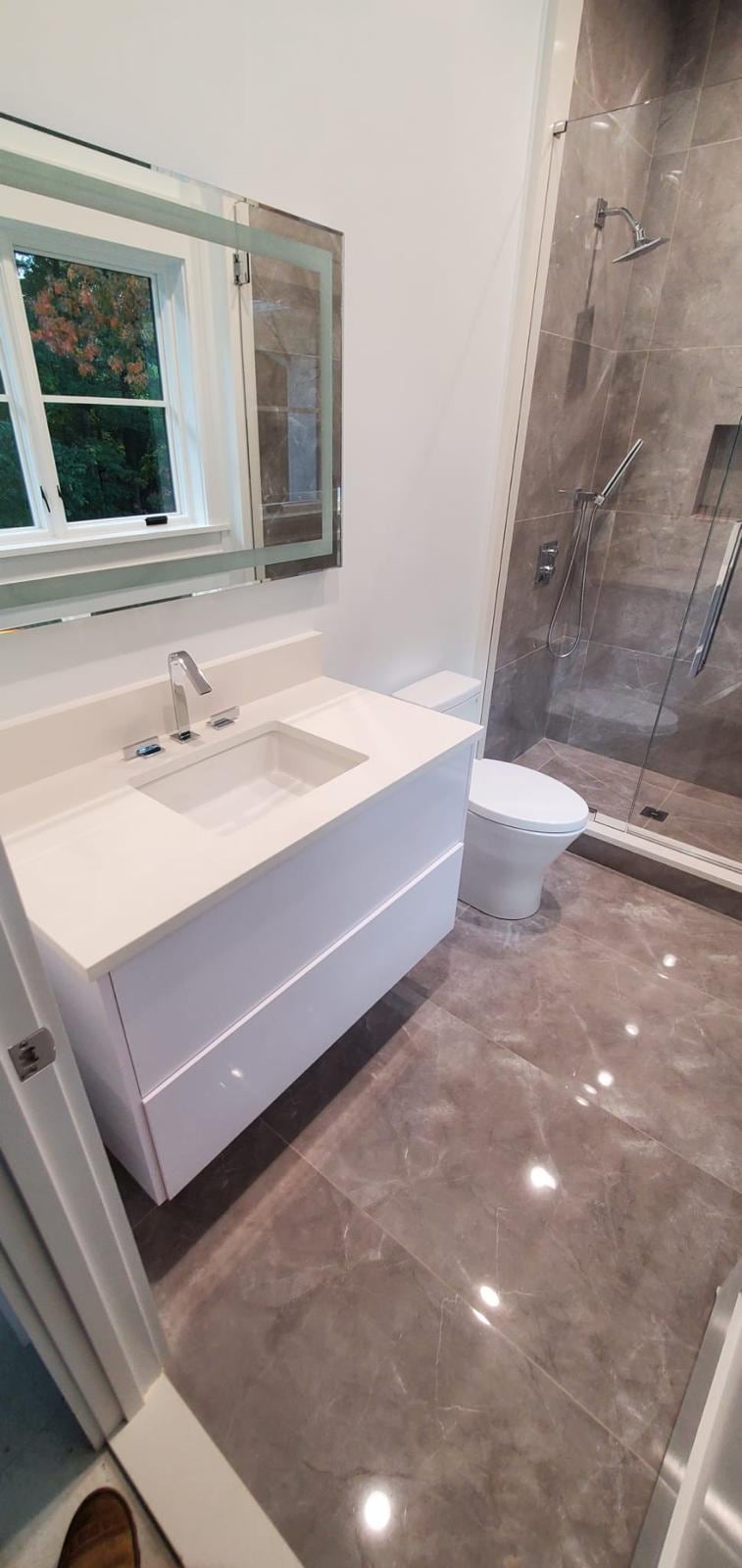 White floating vanity, gray marble-look floor and a glass shower