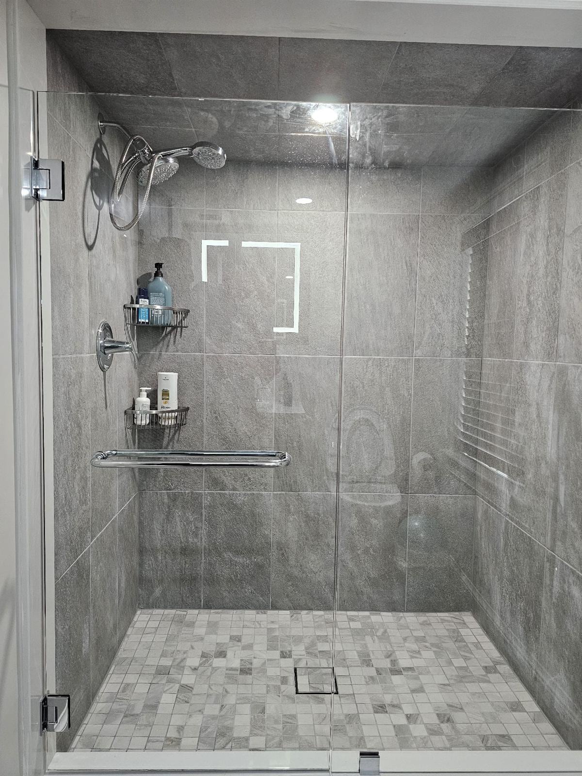 Gray tile shower with glass door and mosaic floor