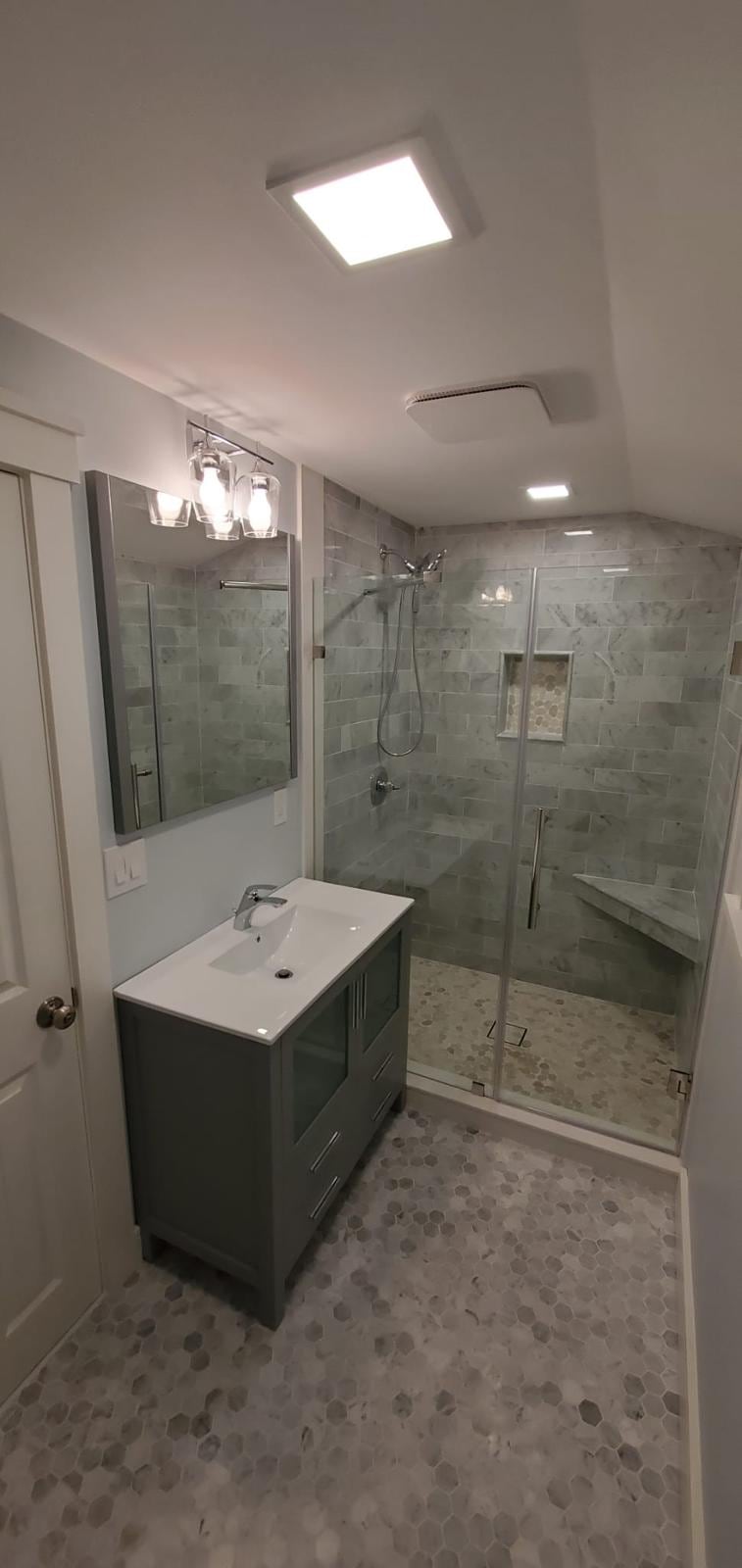 Remodeled bathroom with a gray vanity, glass shower and hexagon tile floor