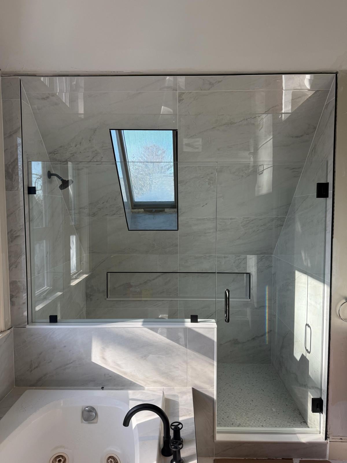 Same bathroom after remodeling: frameless glass shower with marble-look porcelain and a skylight