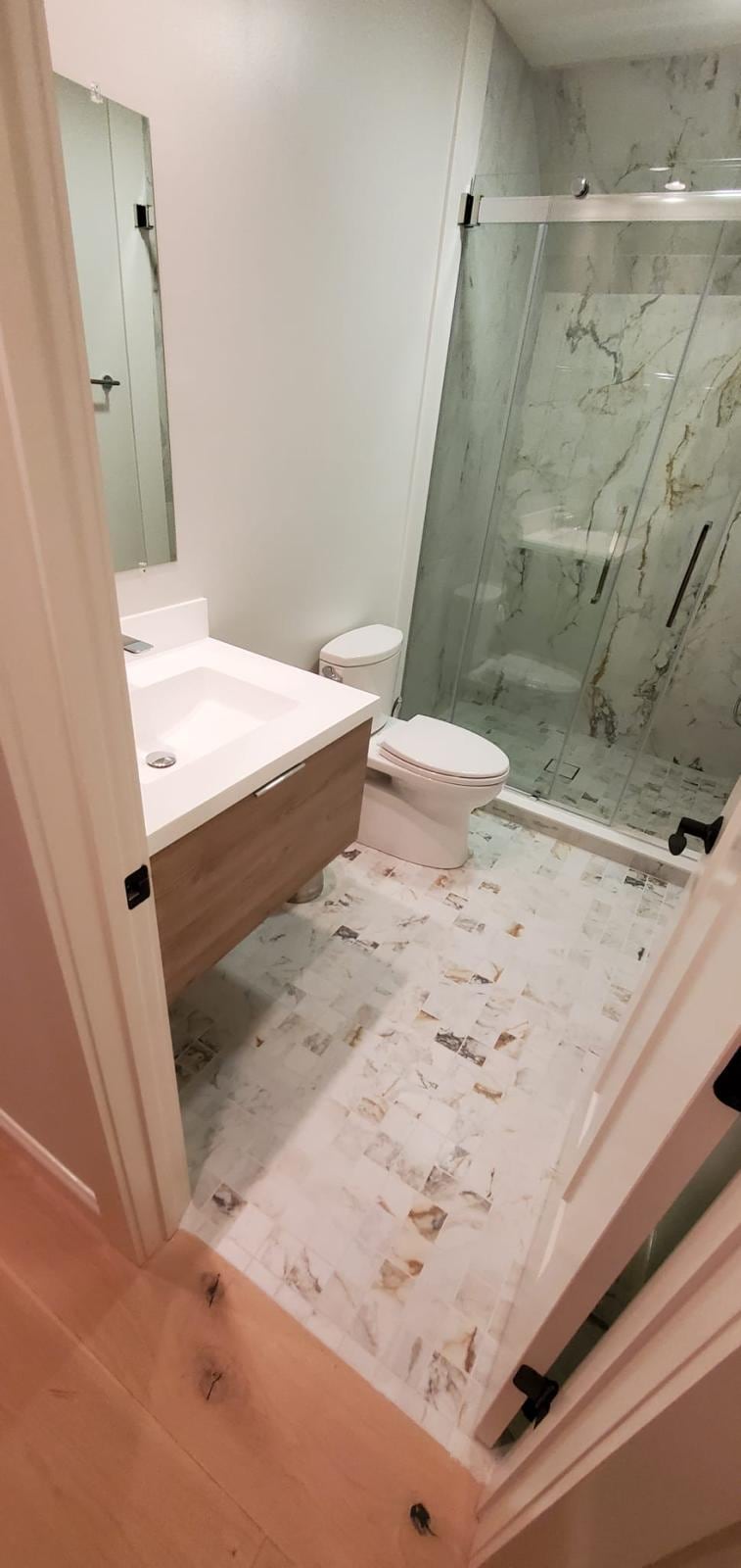 Remodeled bathroom with a wood vanity, glass shower and marble-look tile
