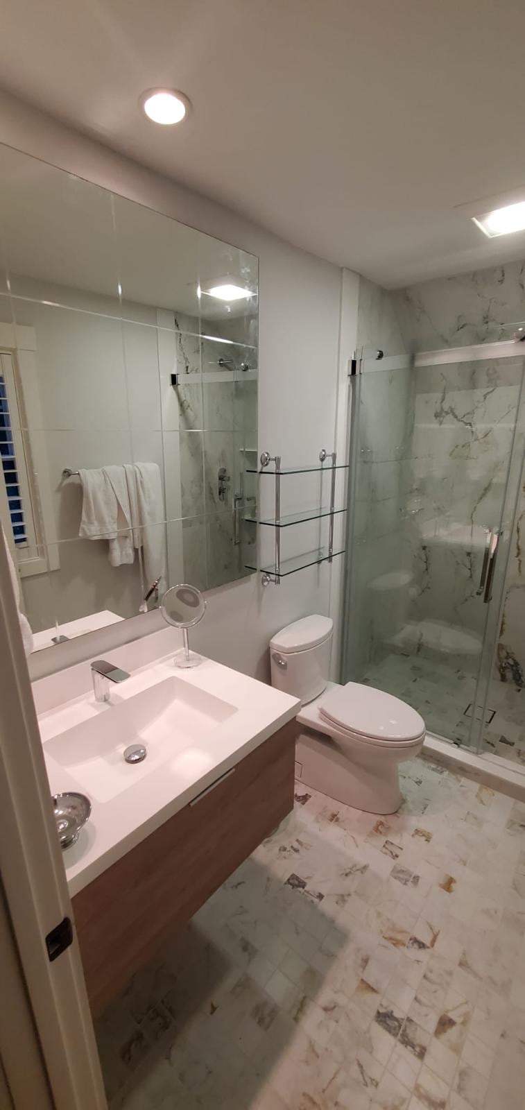 Bathroom with a floating wood vanity, marble-look floor tile and a sliding glass shower