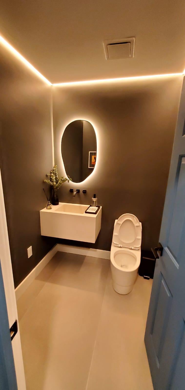 Powder room with dark walls, LED cove lighting, a backlit oval mirror and a floating sink