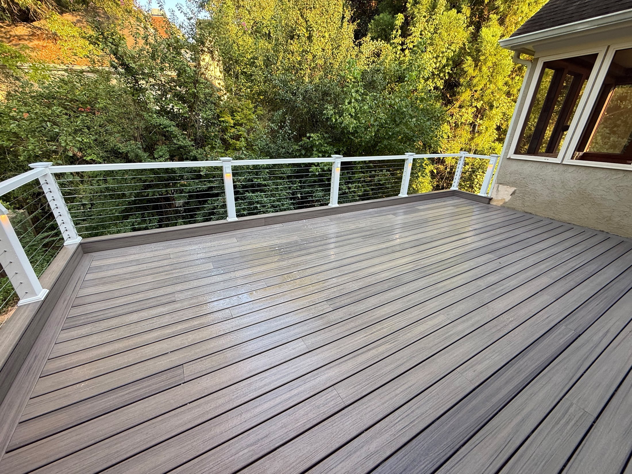 Corner of a gray composite deck with white railing posts and horizontal cable infill