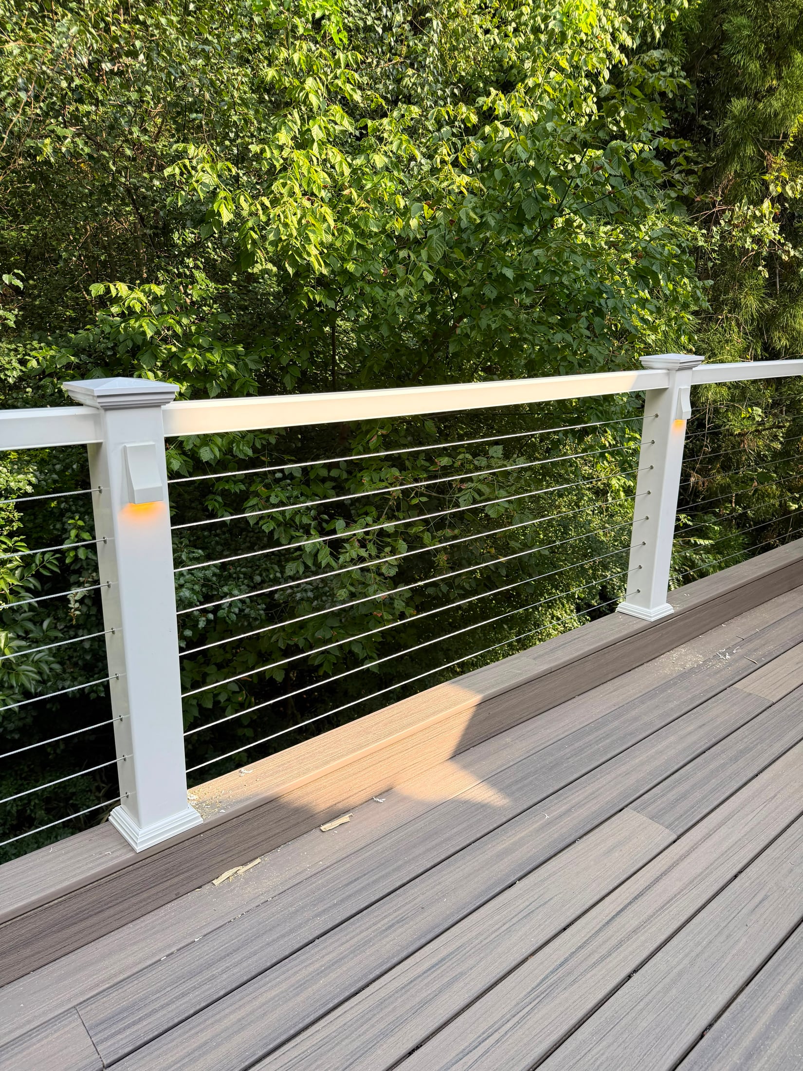 Close view of a white railing post with cable infill at the corner of a composite deck