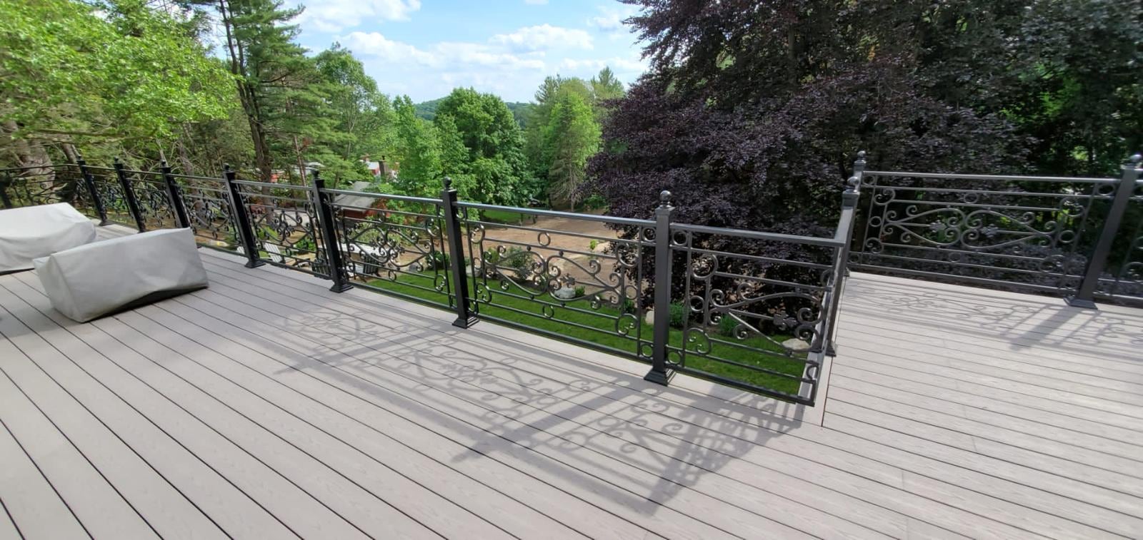 Light gray composite deck with black ornamental metal railing and a view over the treetops