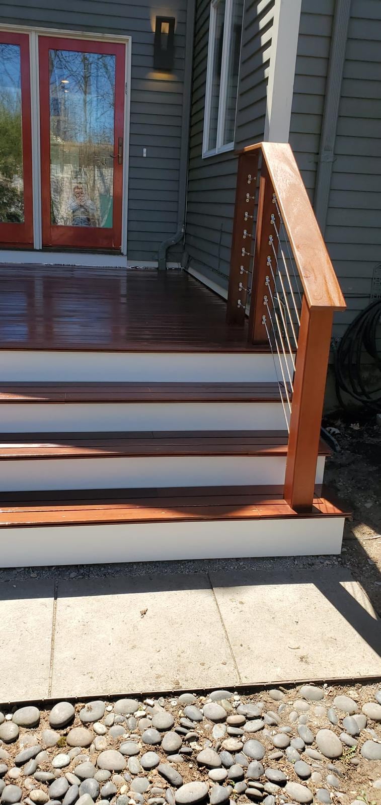 Reddish hardwood deck steps with white risers and a cable railing, next to a door with a red frame