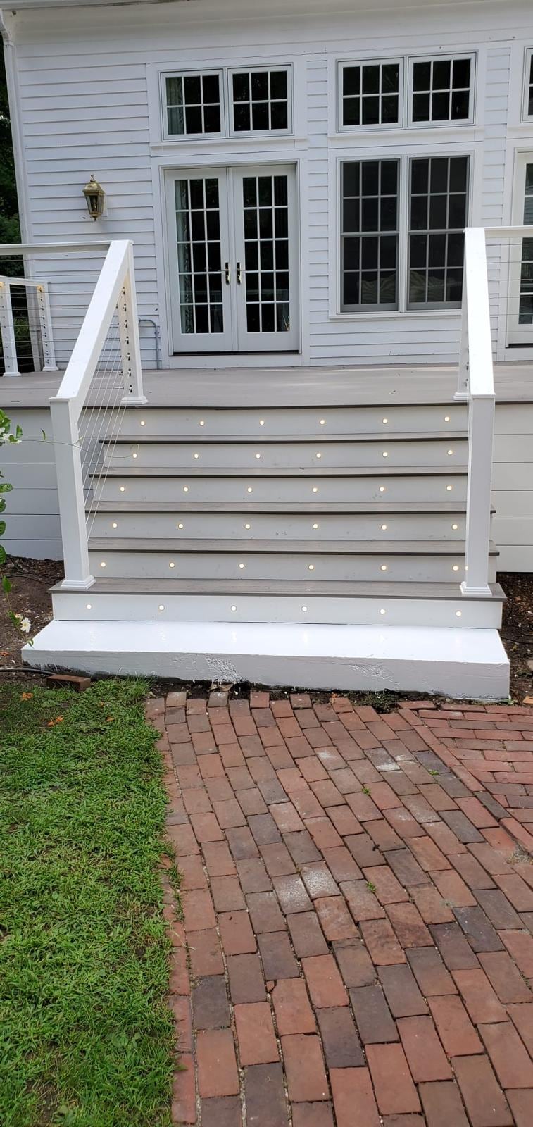 White deck stairs with lights set into each riser, leading from French doors down to a brick walkway