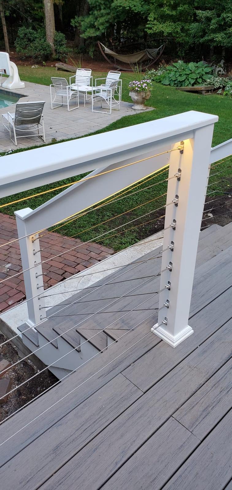 Deck landing with white posts and cable railing overlooking a backyard pool patio