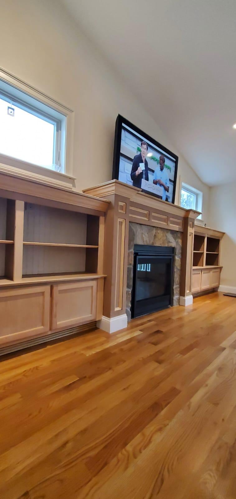 Living room with a custom wood fireplace surround, built-in shelving and hardwood floors