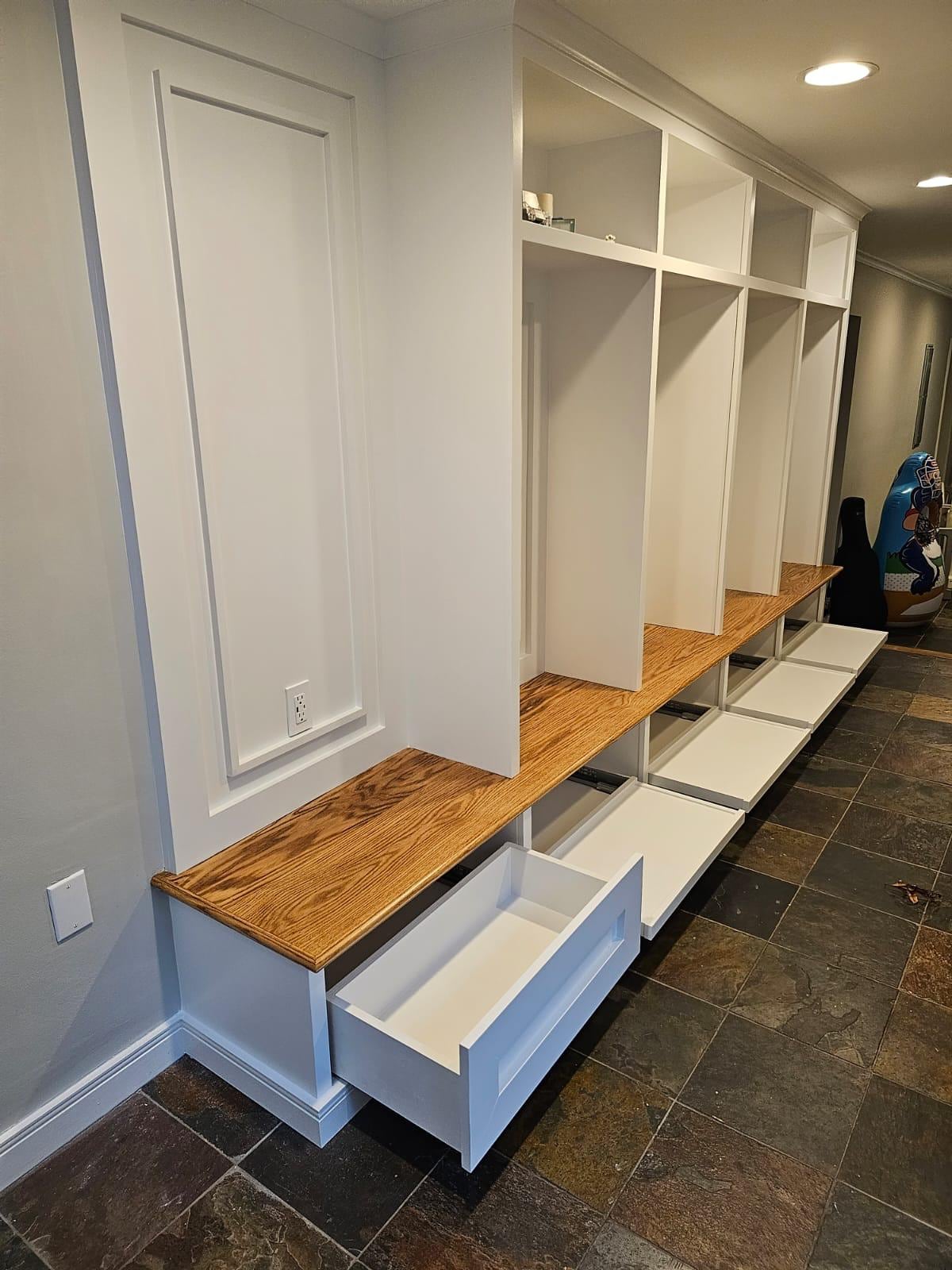Finished white built-in lockers, an oak bench top with pull-out drawers and a slate tile floor