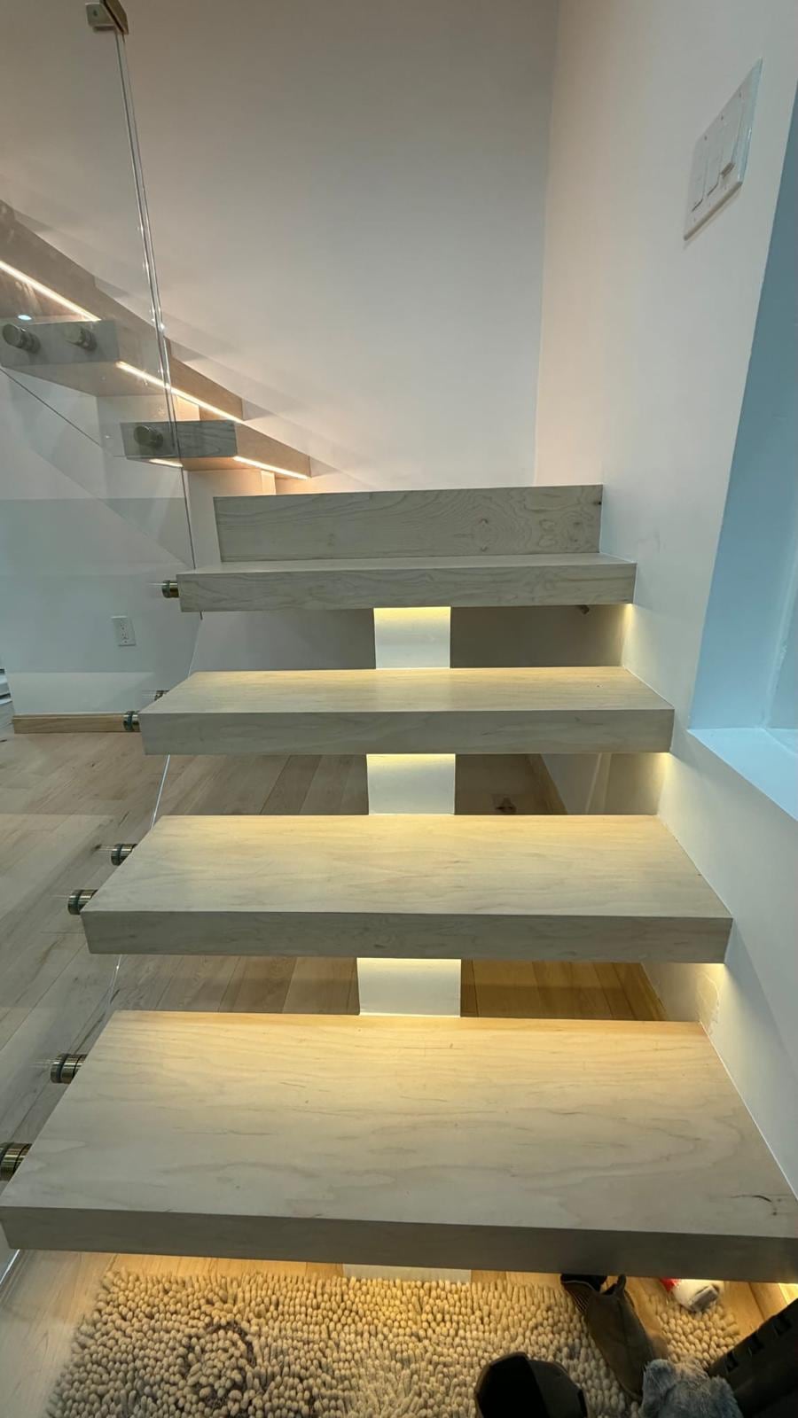 Floating wood stair treads with a glass railing and warm lighting built into the wall beside each step