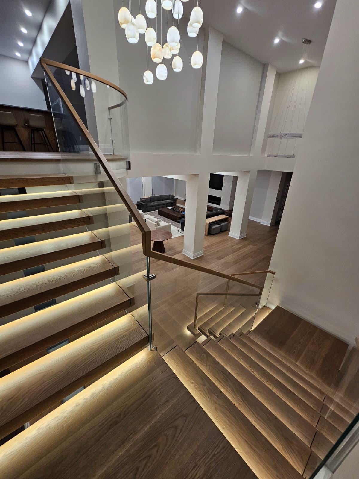 Two-story foyer with lit floating stairs, a glass railing and a cluster pendant light