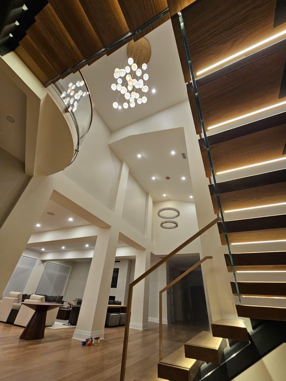 Looking up at a floating staircase with lit treads and a chandelier in a two-story living room
