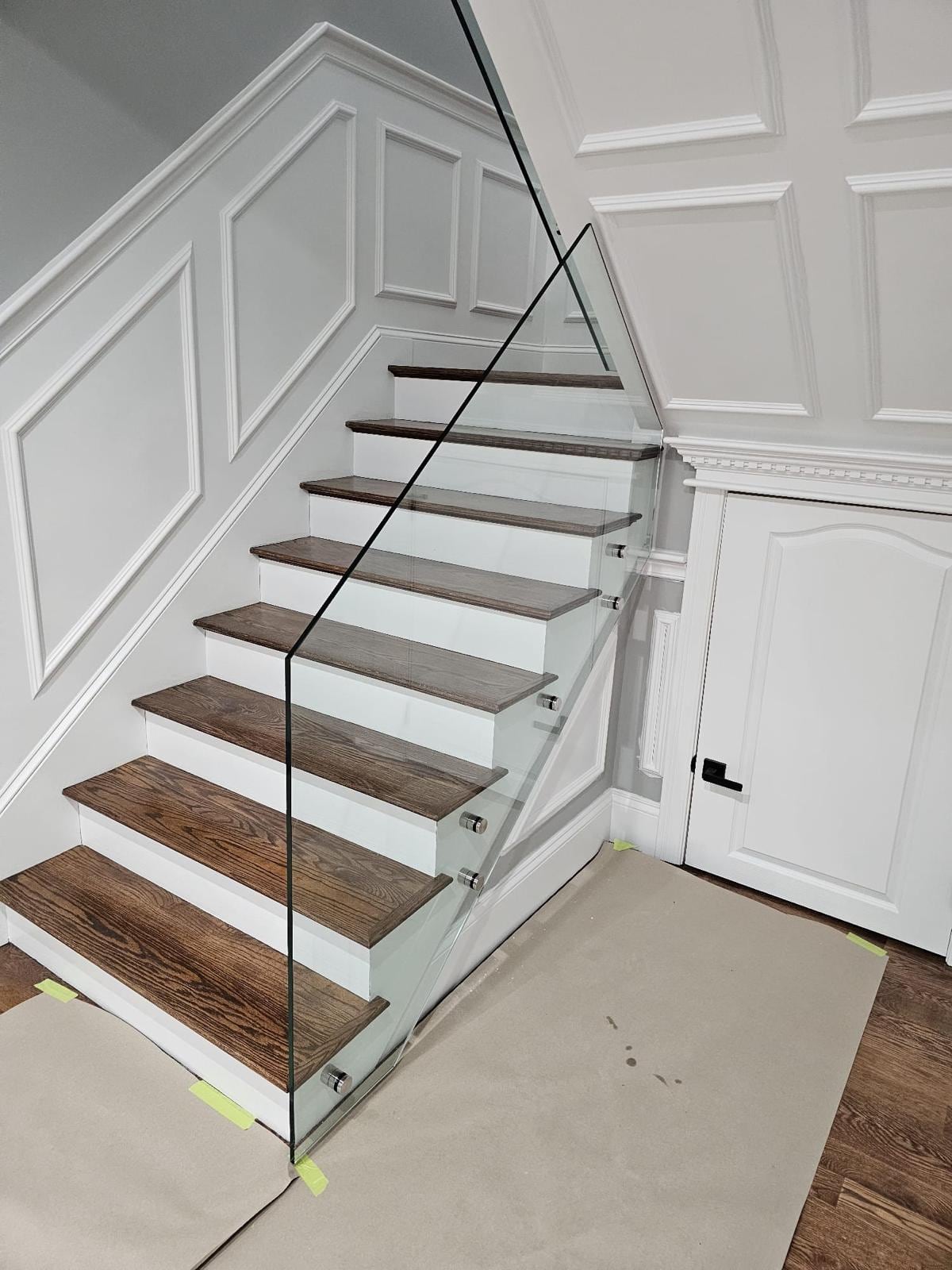 Stairs with wood treads and a glass railing beside white wall paneling