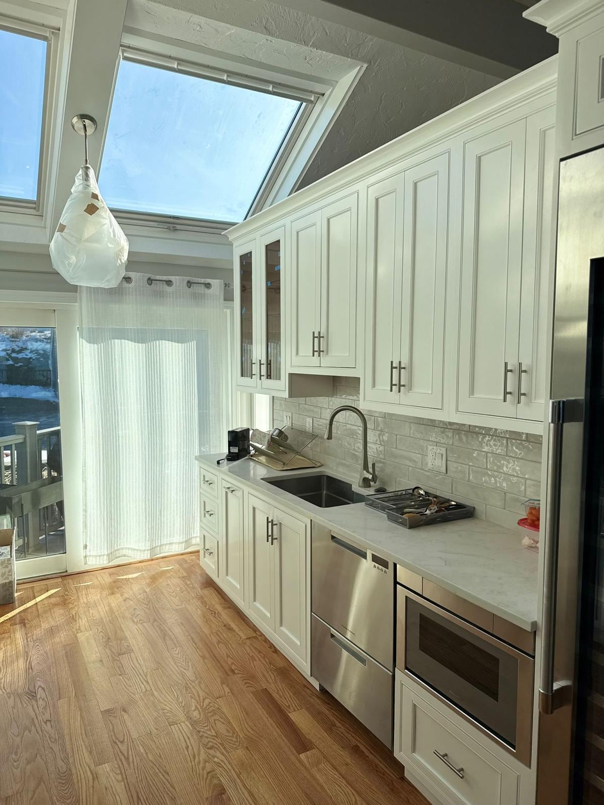 Galley kitchen with white cabinets, subway tile backsplash, a skylight and hardwood floor