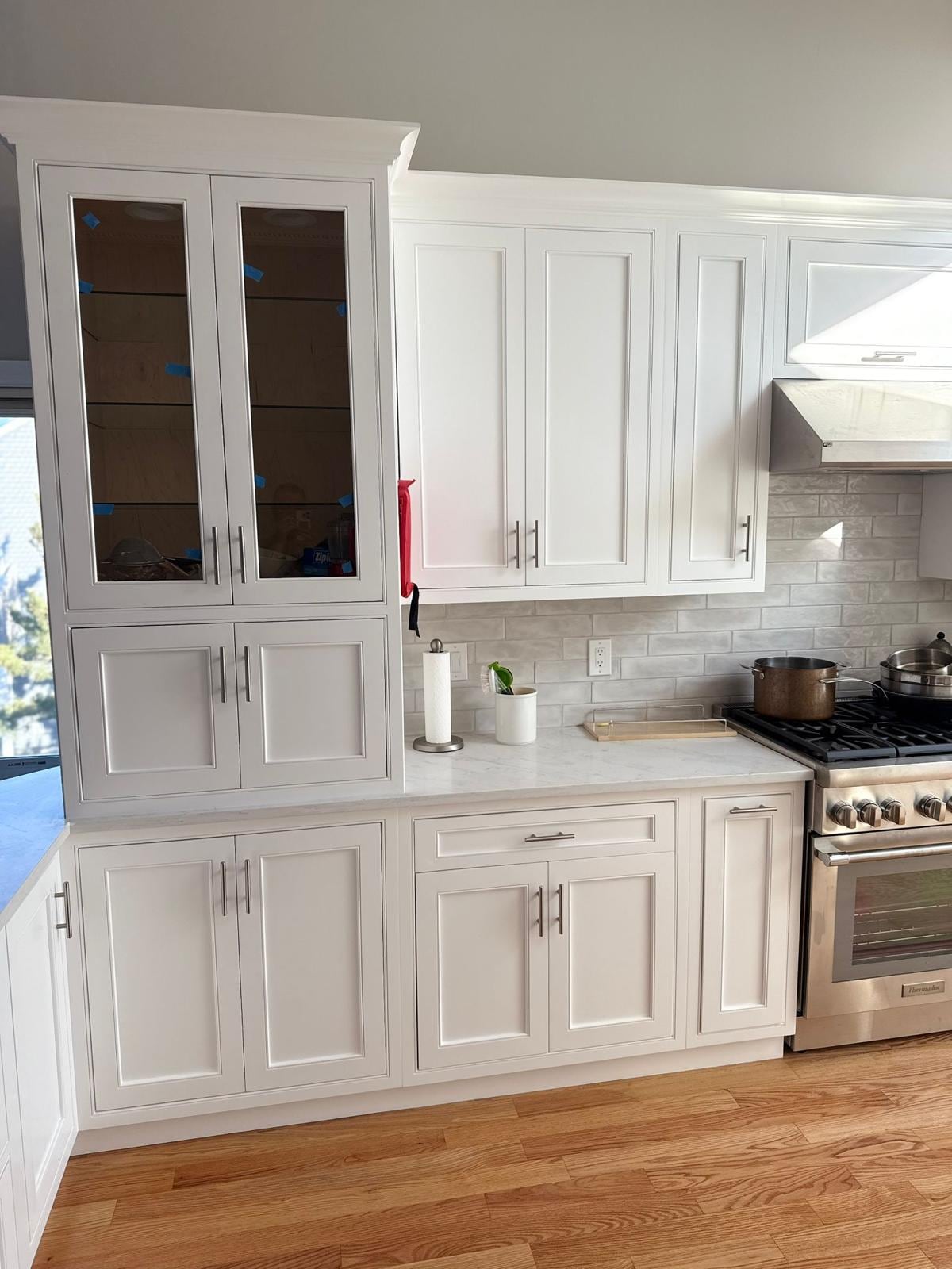 White kitchen cabinets with glass-front upper doors and a gas cooktop under a range hood