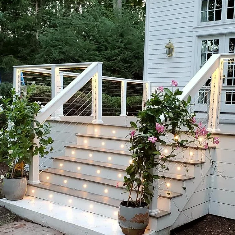 Deck stairs with built-in step lights, white railings with cable infill and potted plants at dusk