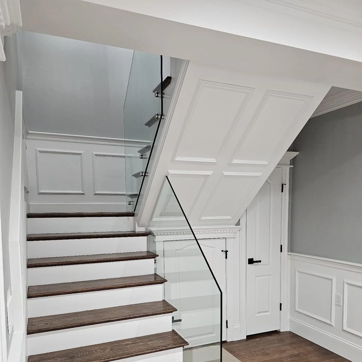 White staircase with wood treads, glass railing and paneled walls