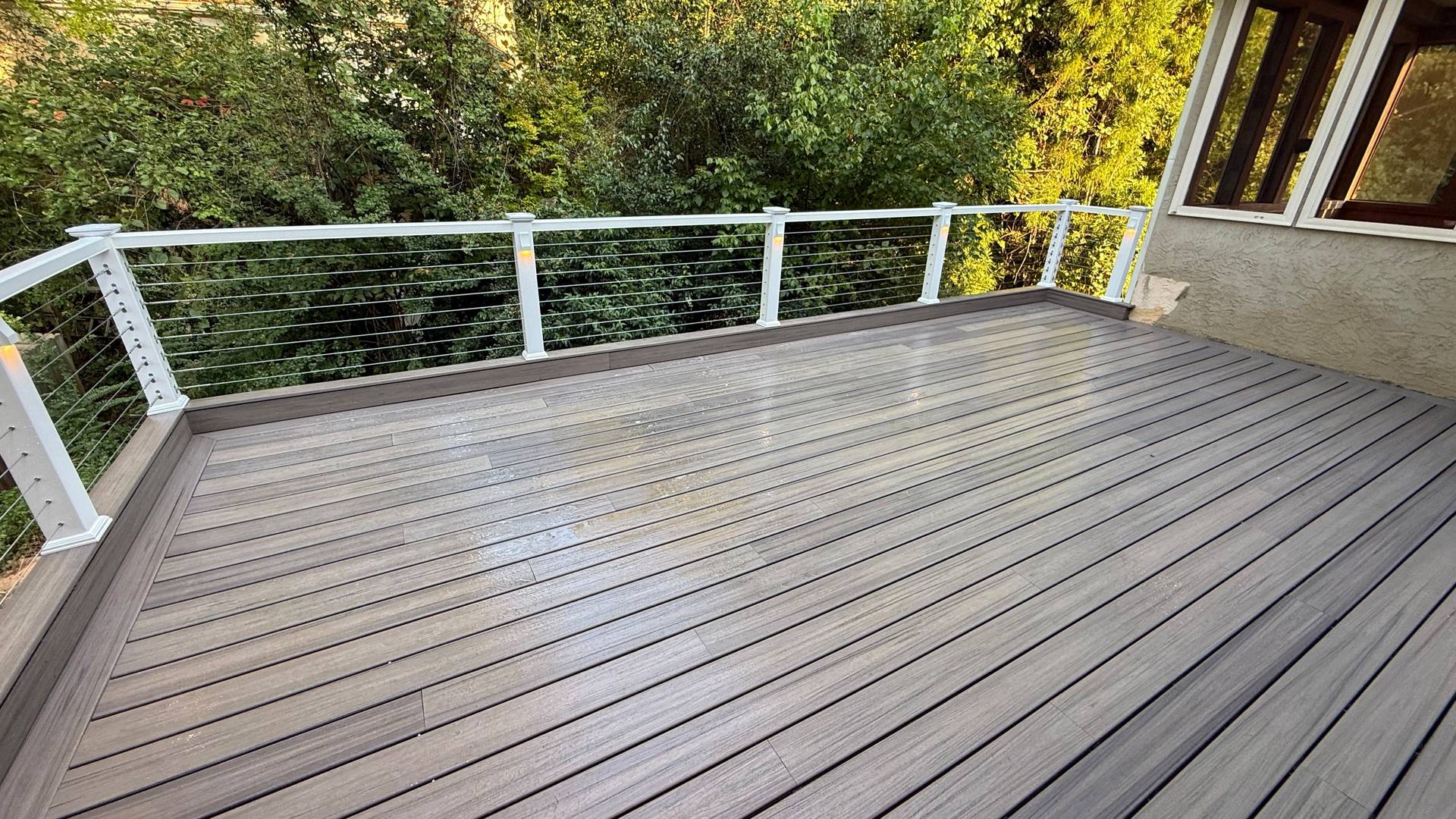 Composite deck with white cable railing beside the house, finished by XPRO Home Improvement