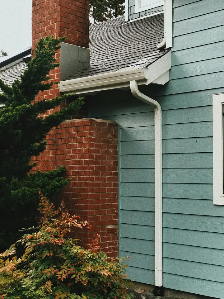 Light blue horizontal lap siding next to a brick chimney, with a white gutter and downspout on a house exterior