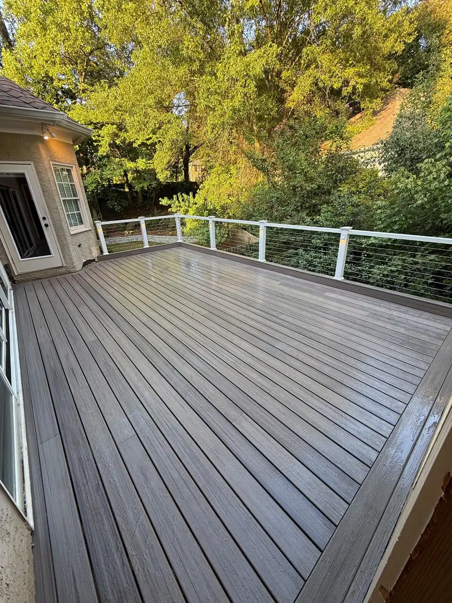 Gray composite deck with white posts and cable railing, seen from the door of the house, trees behind