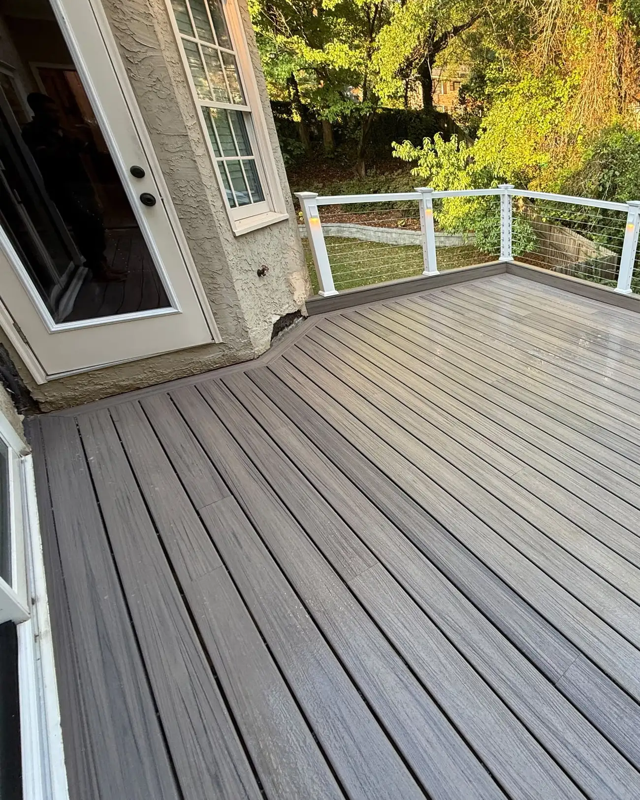 Wide composite deck in gray tones with cable railing along the back edge and woods beyond