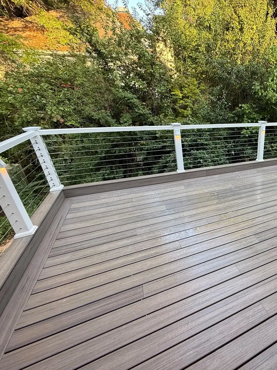 Corner of a gray composite deck with white railing posts and horizontal cable infill