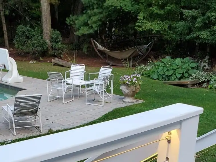 Deck landing with white posts and cable railing overlooking a backyard pool patio