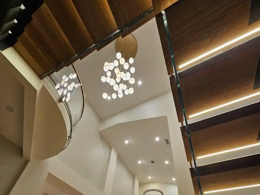 Looking up at a floating staircase with lit treads and a chandelier in a two-story living room
