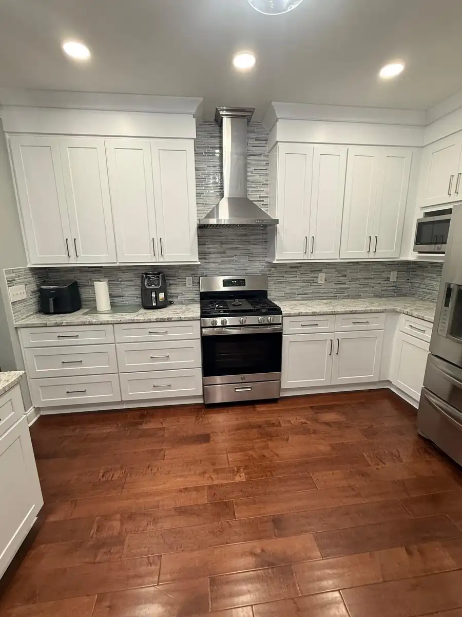 Kitchen after remodeling: white shaker cabinets, mosaic tile backsplash and a stainless wall hood