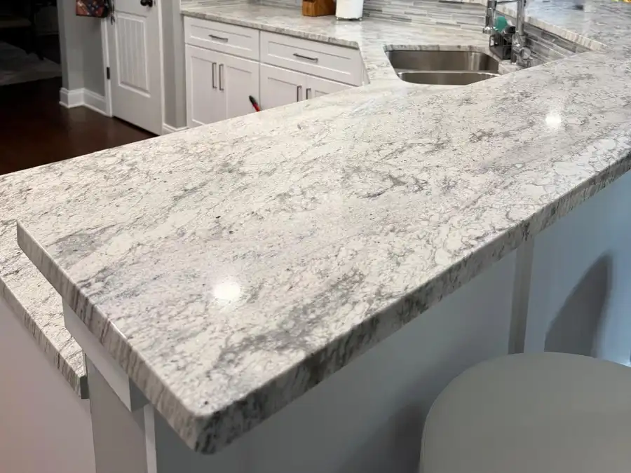 Kitchen peninsula after remodeling, with light granite, white cabinets and glass tile backsplash