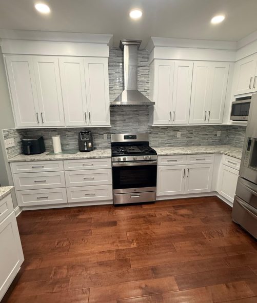 Kitchen after remodeling: white shaker cabinets, mosaic tile backsplash and a stainless wall hood